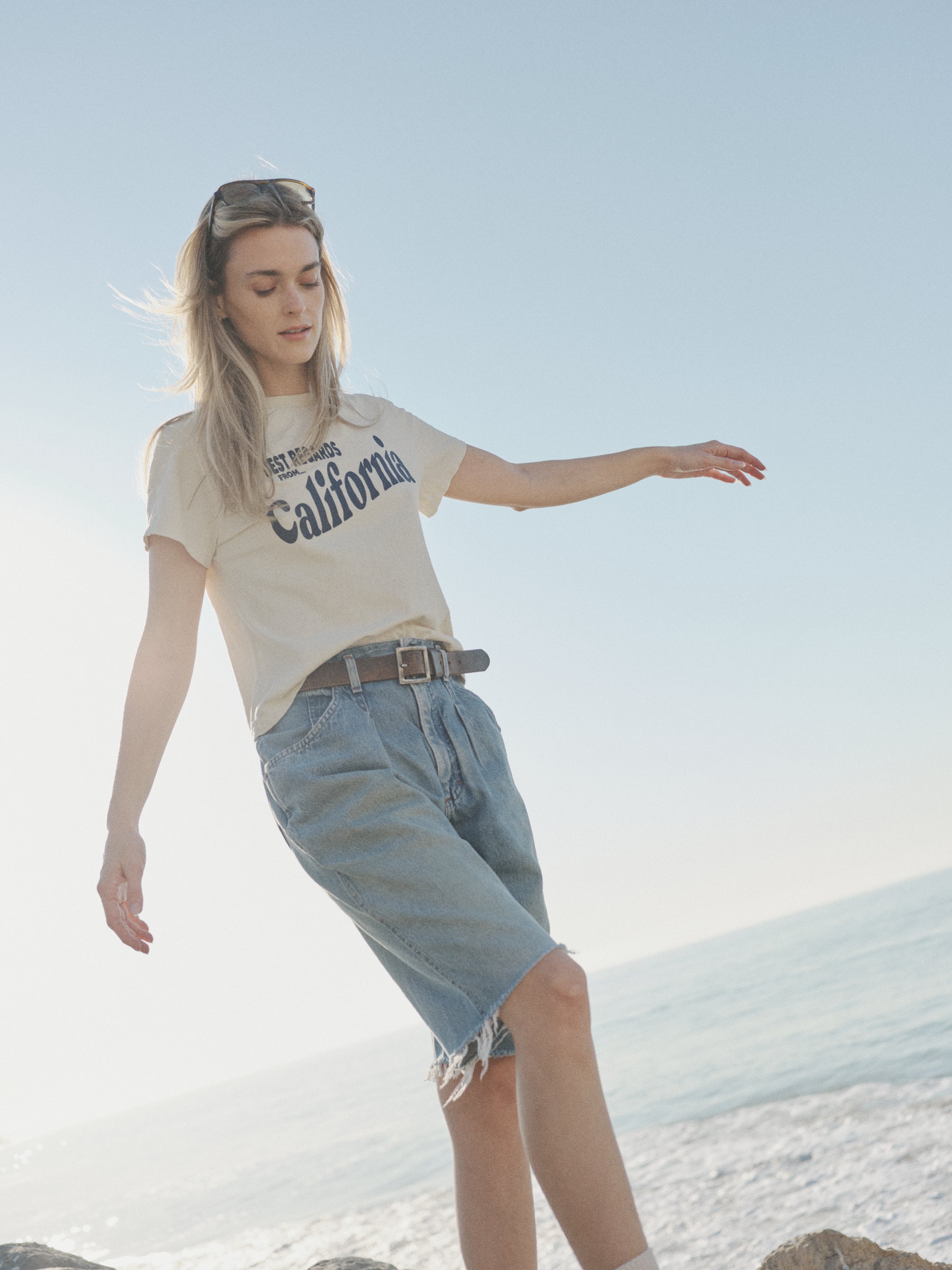Woman standing on a beach wearing a 'California' t-shirt and denim shorts.
