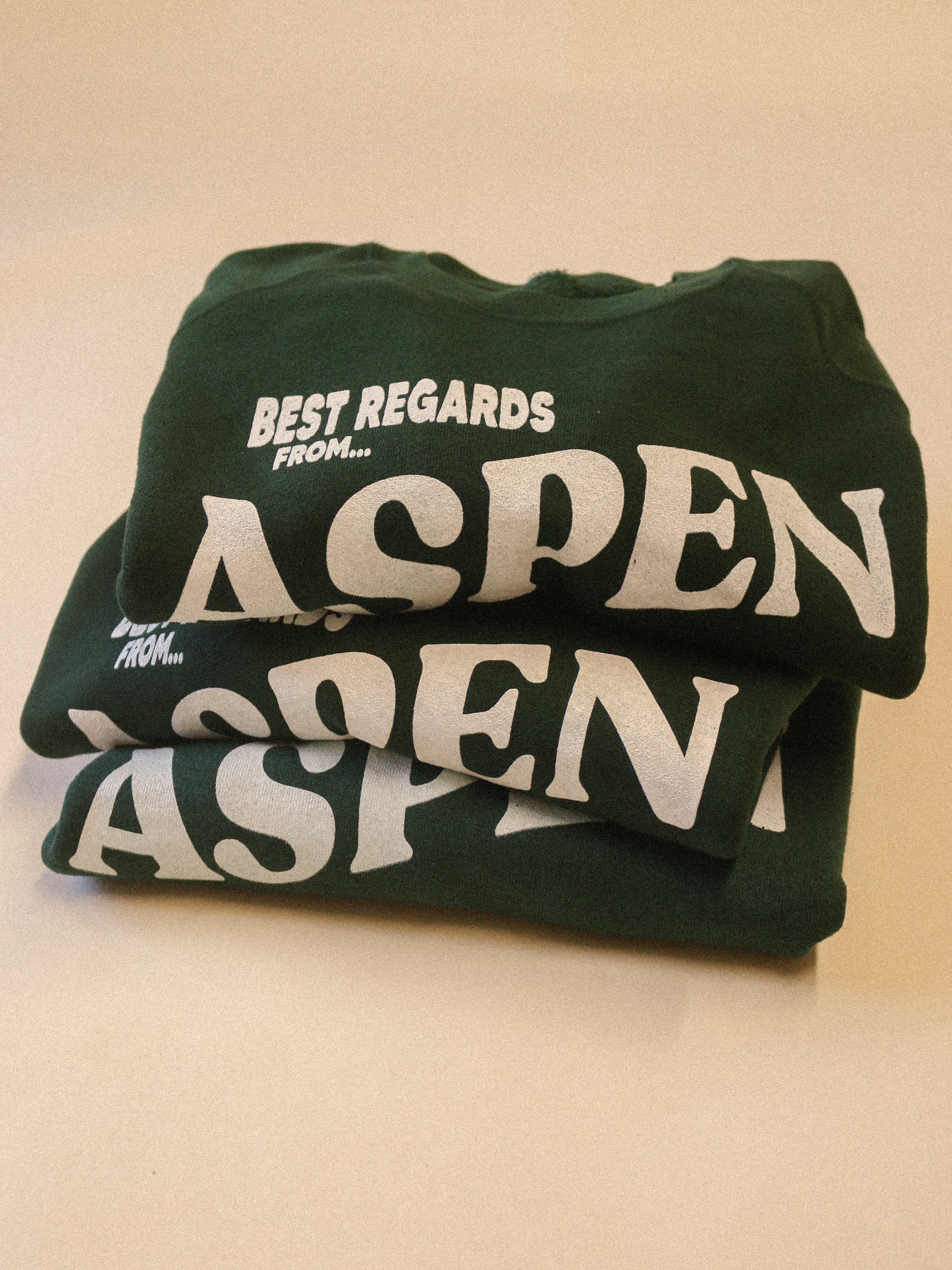 Green sweatshirt with 'Best Regards From Aspen' text on a beige background