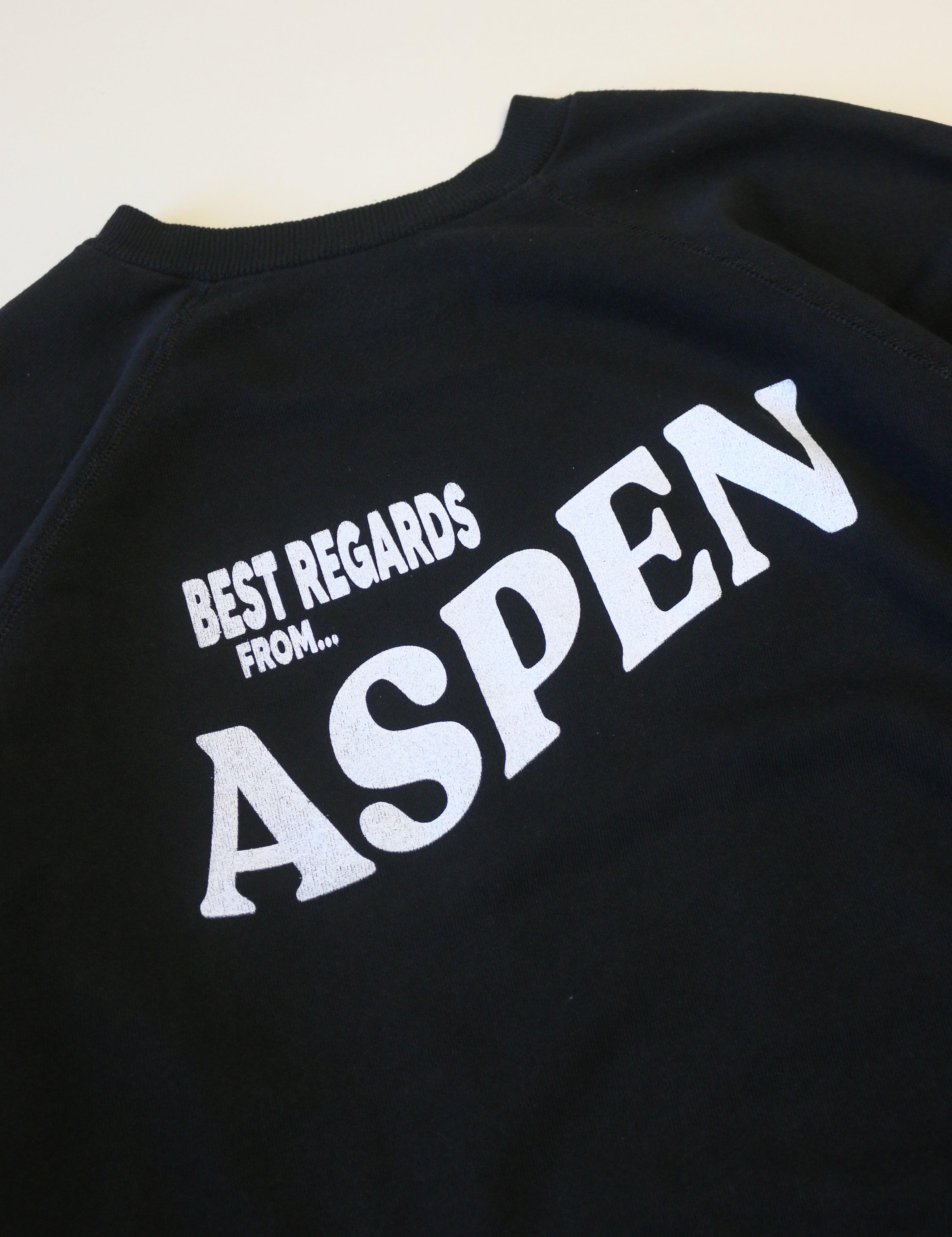 Black sweatshirt with 'Best Regards from Aspen' text on a beige background