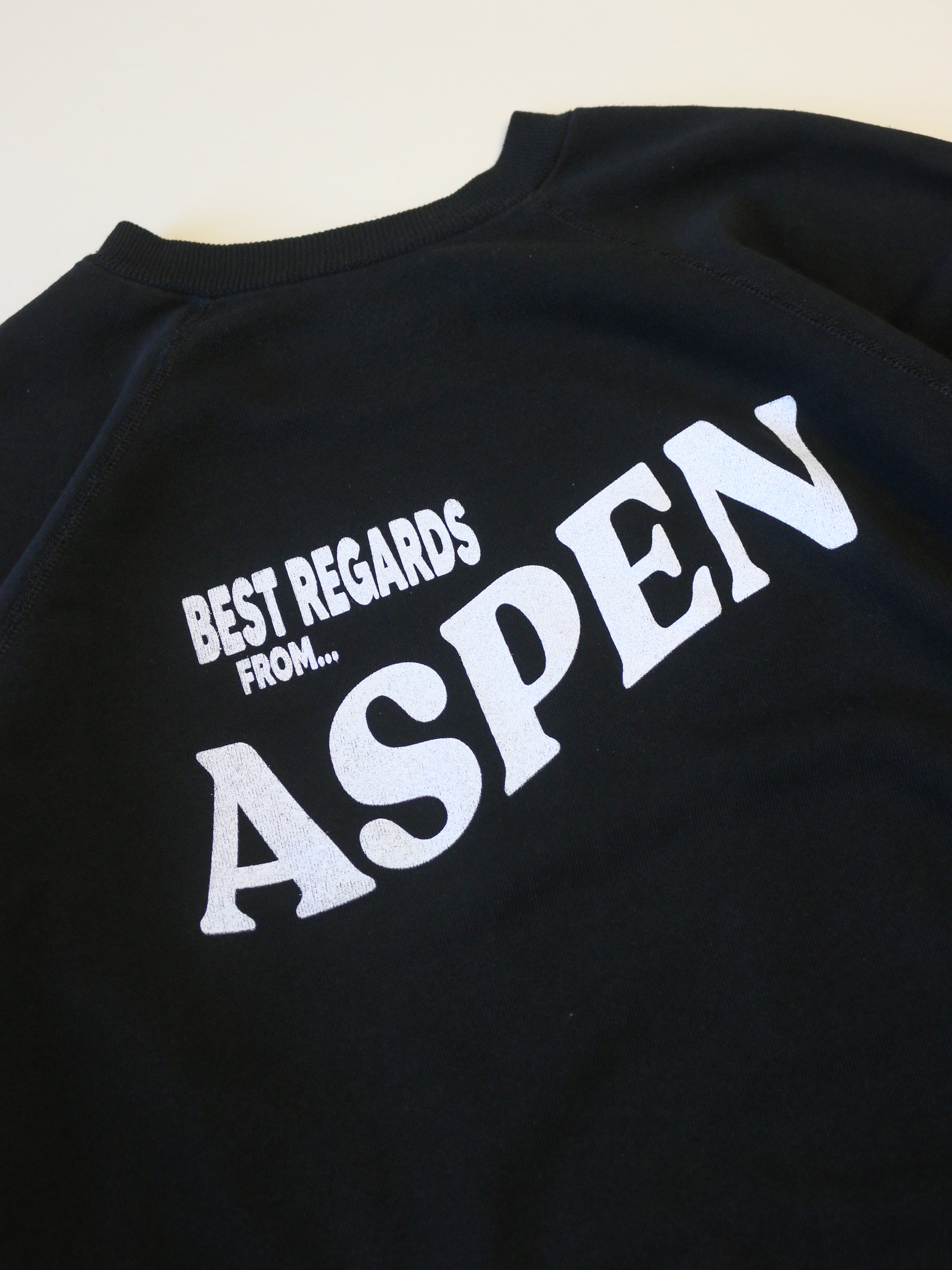 Black sweatshirt with 'Best Regards from Aspen' text on a beige background